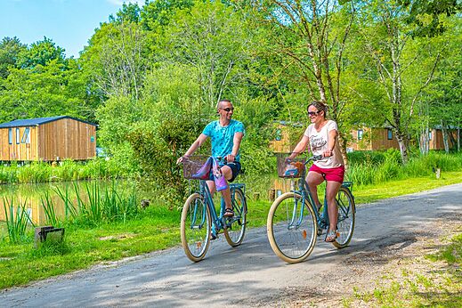 Paar beim Radfahren auf grünem Weg am Teich auf Camping CAPFUN La Rivière in Valence-en-Poitou (86).
