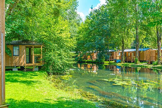 Holzunterkünfte am Flussufer, auf dem Campingplatz CAPFUN La Rivière in Valence-en-Poitou (86).