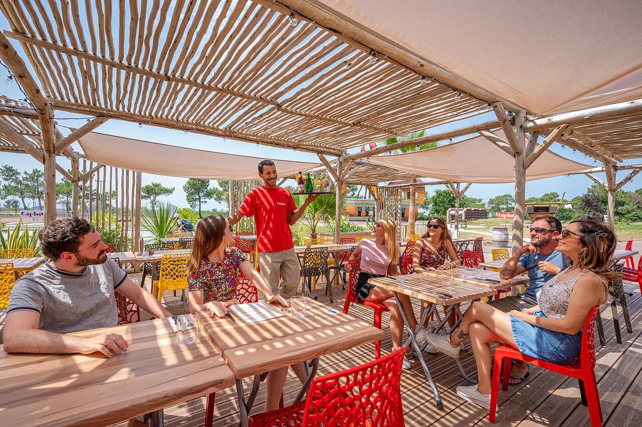 Shaded restaurant and bar terrace, guests served at CAPFUN Roumingue campsite in LANTON (33).