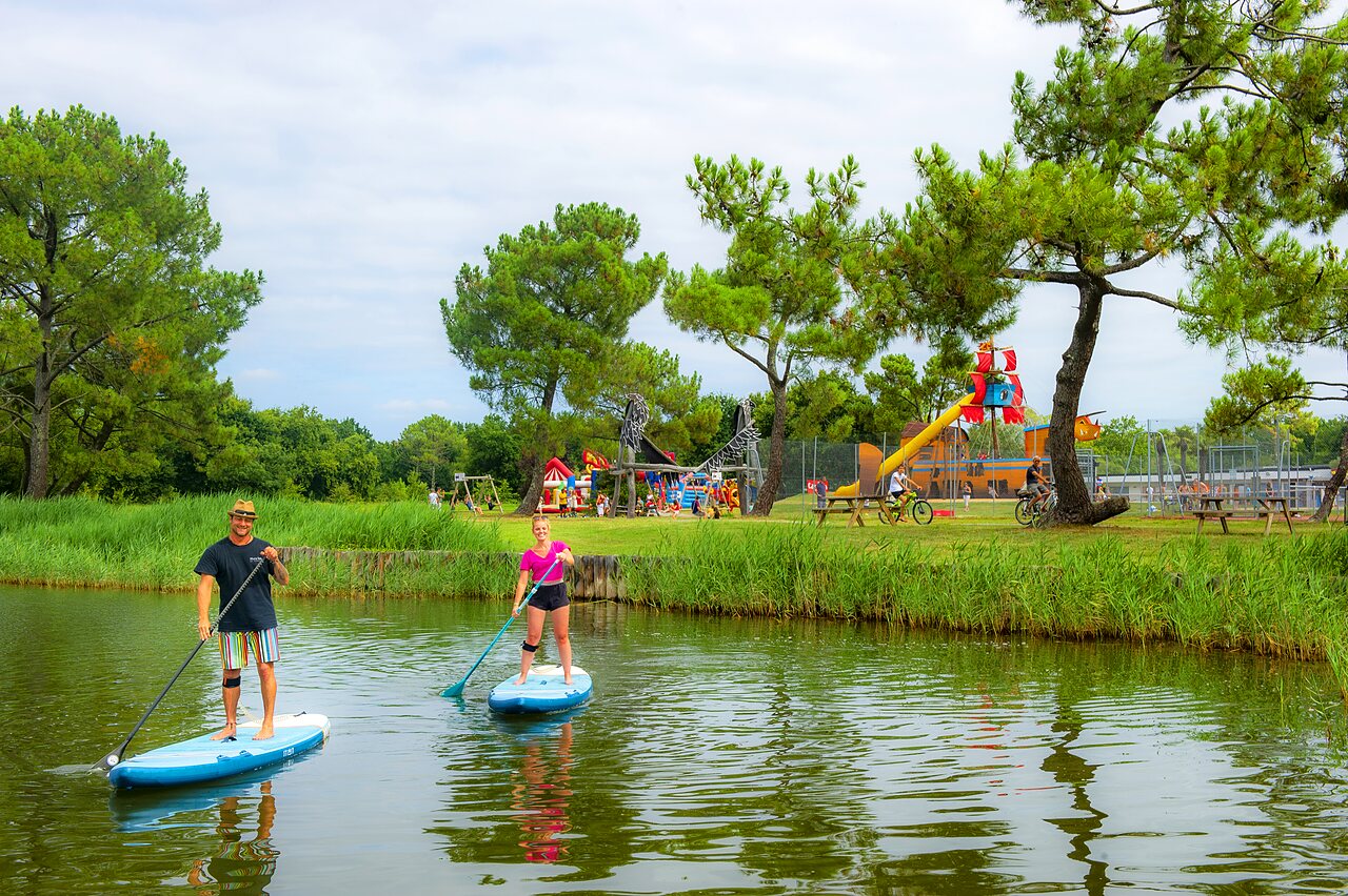 Paddleboarders on water, children's playground at CAPFUN Roumingue campsite in LANTON (33).