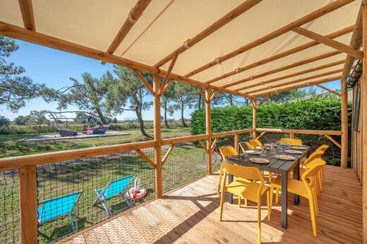 Überdachte Terrasse eines Mobilheims mit Tisch und gelben Stühlen bei CAPFUN Roumingue.