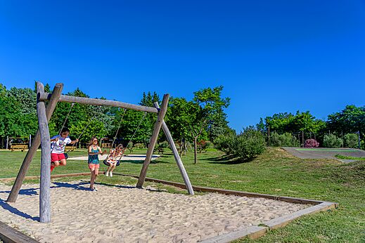 Houten schommel met kinderen spelend in het zand op camping CAPFUN Soubeyranne in REMOULINS (30).