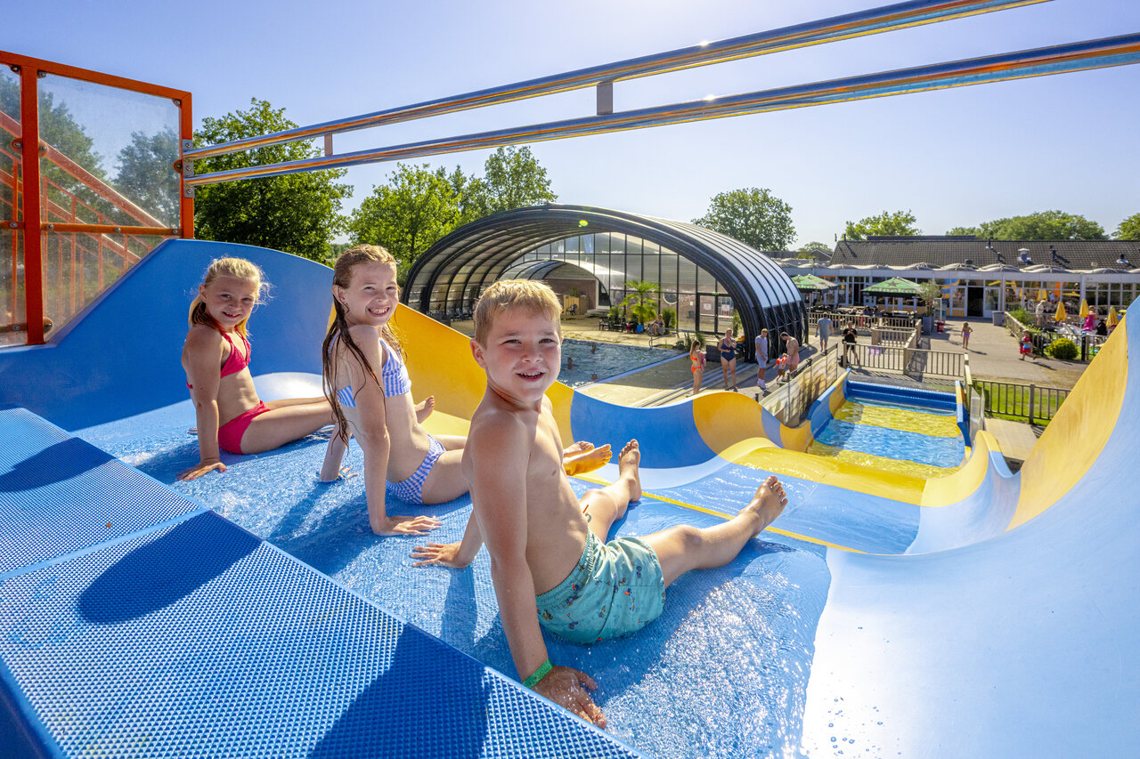 Lachende Kinder auf blau-gelber Wasserrutsche, Campingplatz CAPFUN De Sprookjescamping in Rheeze.