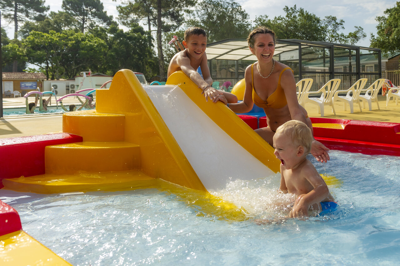 Children and family on water slide in pool at CAPFUN Sud Land campsite.