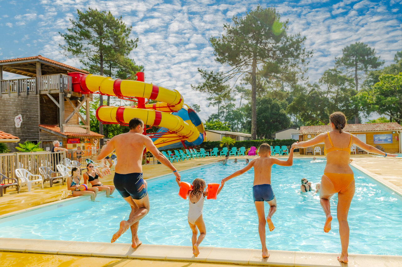 Family jumping into swimming pool with giant waterslides at CAPFUN Sud Land campsite in Labenne-Ocean.