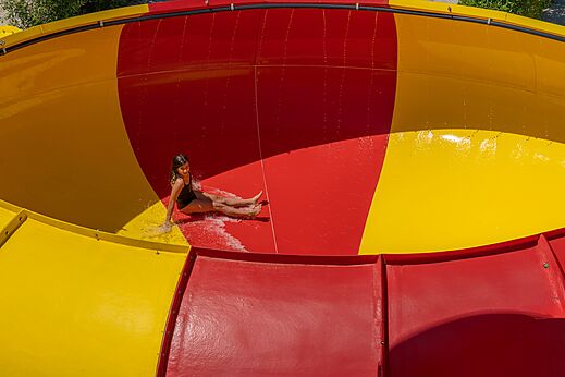 Fille glissant sur toboggan aquatique rouge et jaune au camping CAPFUN Talaris Vacances à Lacanau (33).