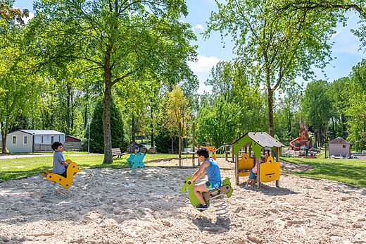 Enfants jouant sur des jeux à ressort dans l'aire de jeux au camping CAPFUN Tensch Jolie à Grostenquin (57).