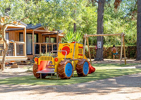 Kinderspielplatz mit Traktor und Schaukel neben Mobilheimen auf dem Campingplatz CLICOCHIC Texas in Argelès sur Mer (66).