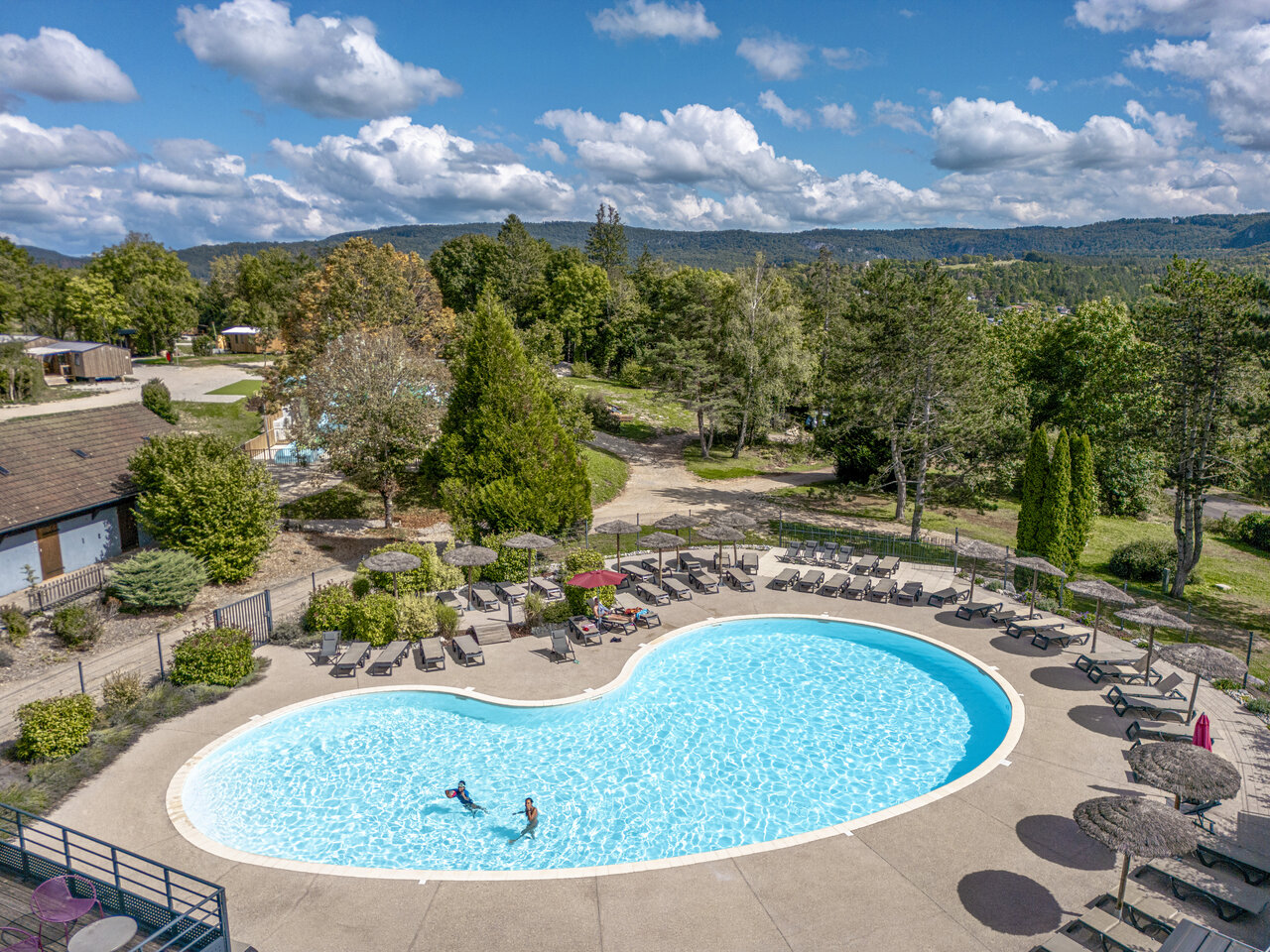Large outdoor swimming pool with sun loungers and parasols, aerial view at CLICOCHIC Trelachaume campsite in Maisod (39).