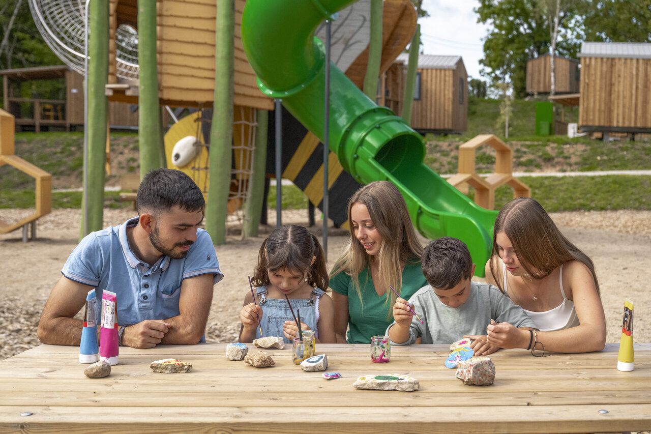 Family painting rocks, playground slide at CLICOCHIC Trelachaume campsite in Maisod (39).