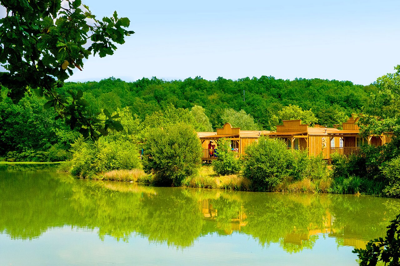 Western themed mobile homes and lake at CAPFUN Ullule campsite in Tournon d'Agenais (47).