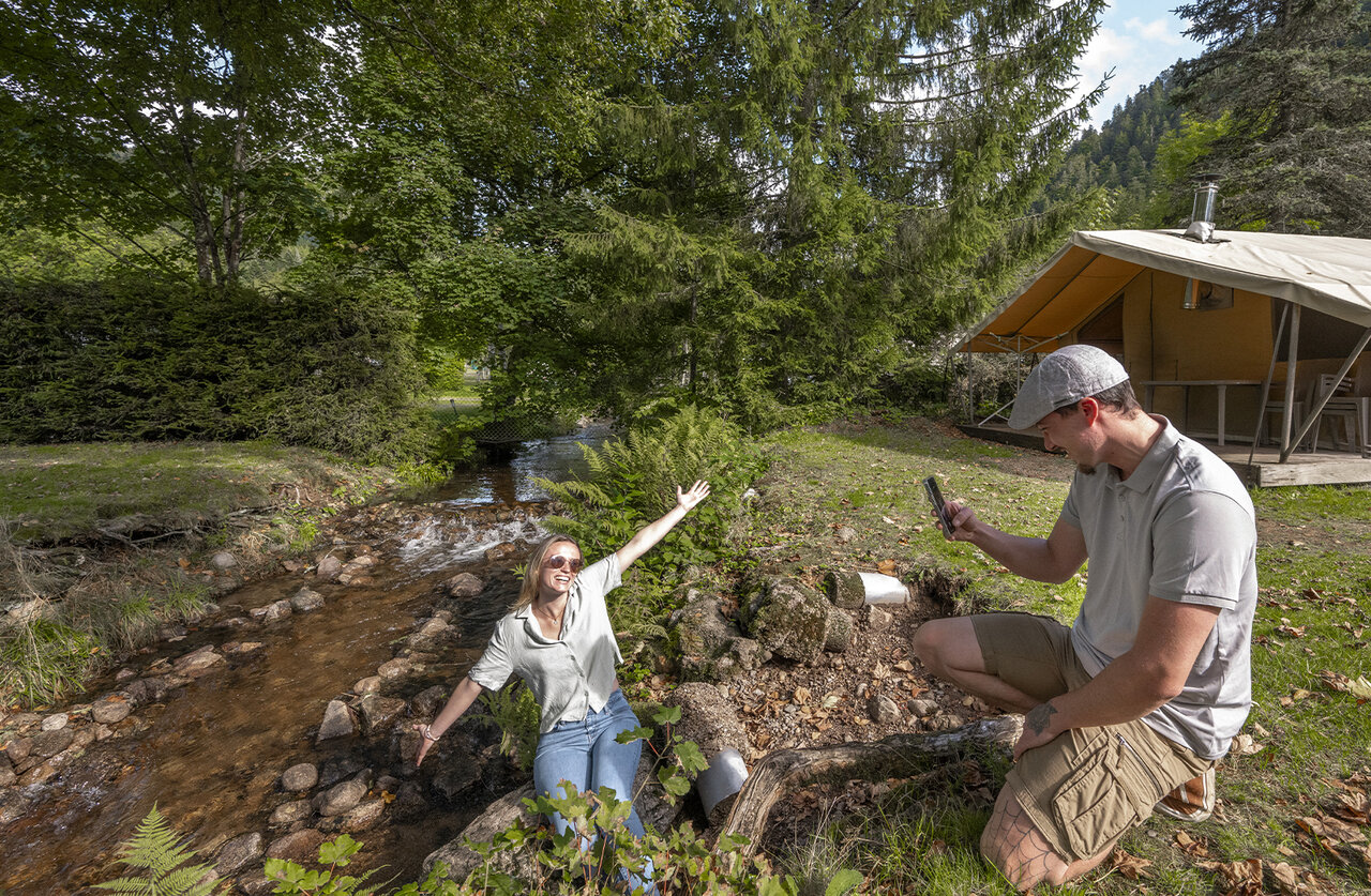 Couple pr�s d'un ruisseau, tente safari au camping CLICOCHIC Verte Vall�e, XONRUPT LONGEMER.