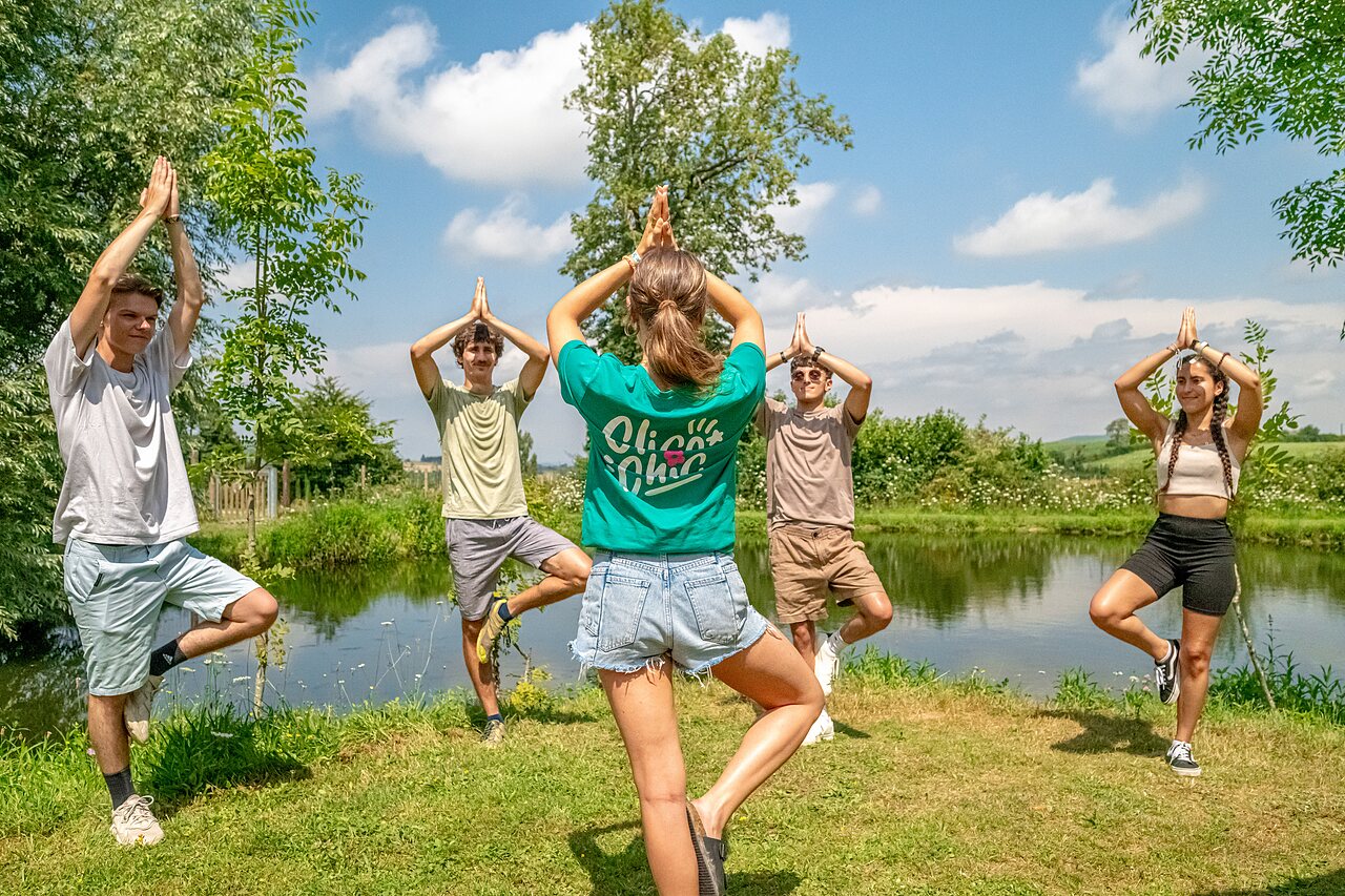Grupo practicando yoga al aire libre junto a un estanque en el camping CLICOCHIC Village des Meuniers en Dompierre-les-Ormes.