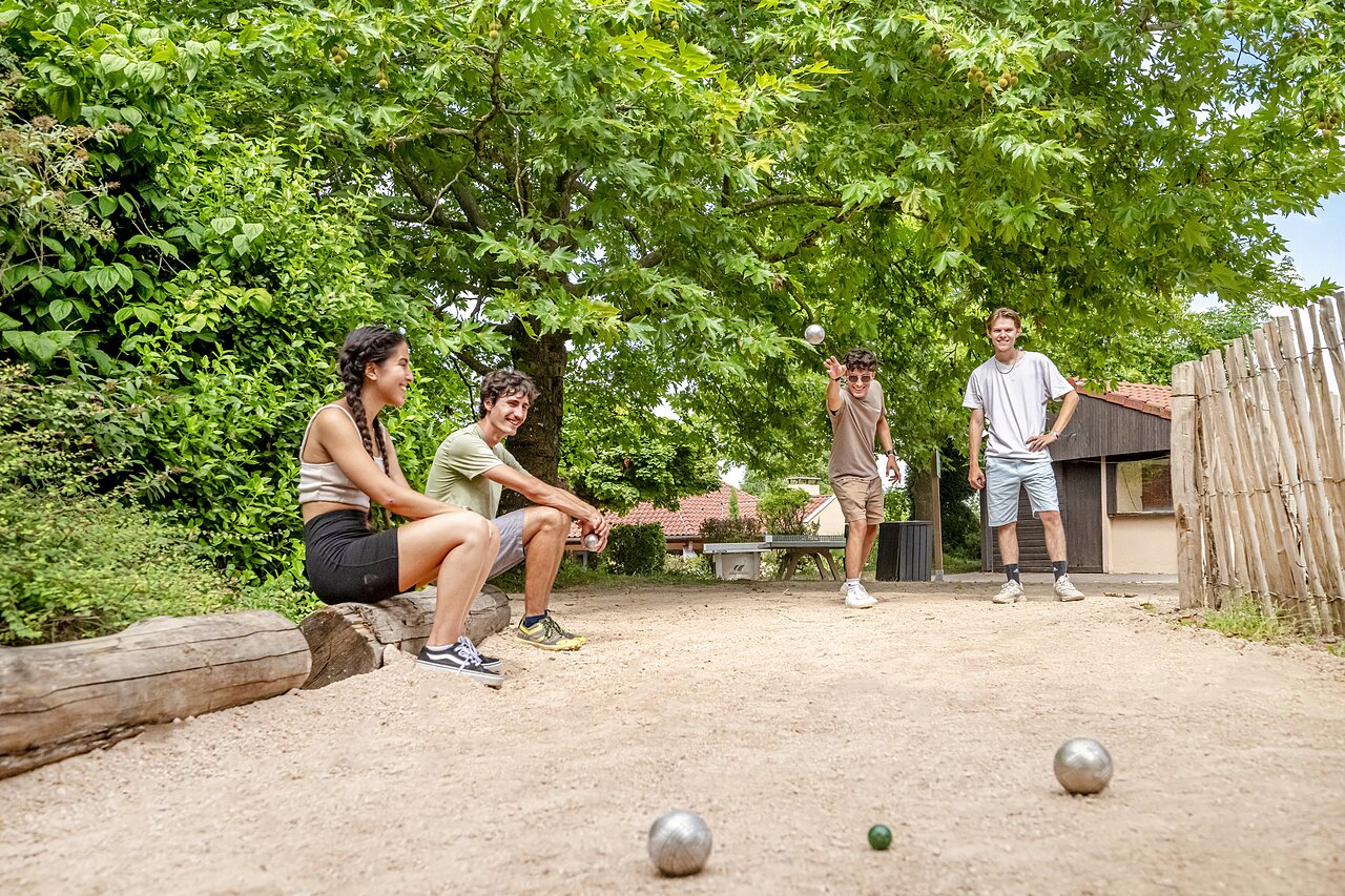 J�venes jugando a la petanca en una cancha sombreada en el camping CLICOCHIC Village des Meuniers en Dompierre-les-Ormes (71).