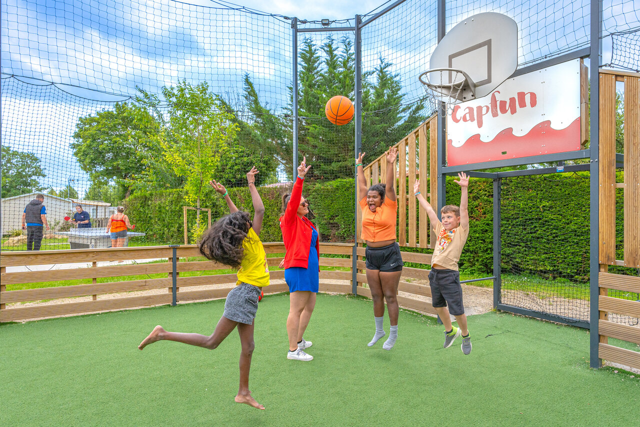Kinder und Erwachsene spielen Basketball auf Multisportplatz auf dem Campingplatz CAPFUN Le Village Parisien in VARREDDES (77).