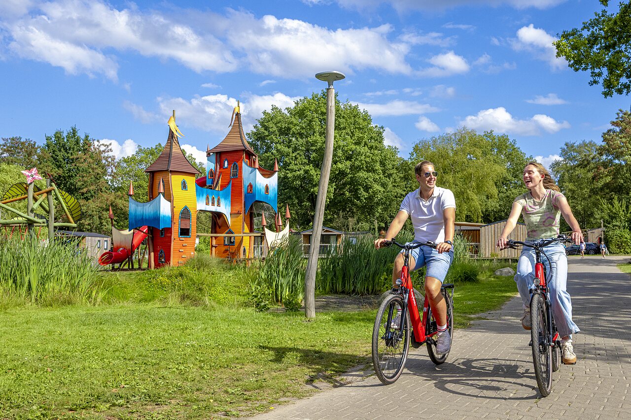 Bunter Burgspielplatz und Rad fahrendes Paar auf Camping CAPFUN Vlinderloo in Enschede.