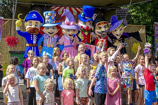 Kleurrijke mascottes en blije kinderen tijdens animatie op camping CAPFUN Vlinderloo in Enschede.