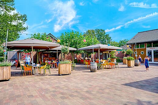Außenterrasse des Restaurants mit Tischen und Sonnenschirmen auf dem Campingplatz CAPFUN Wieskamp.
