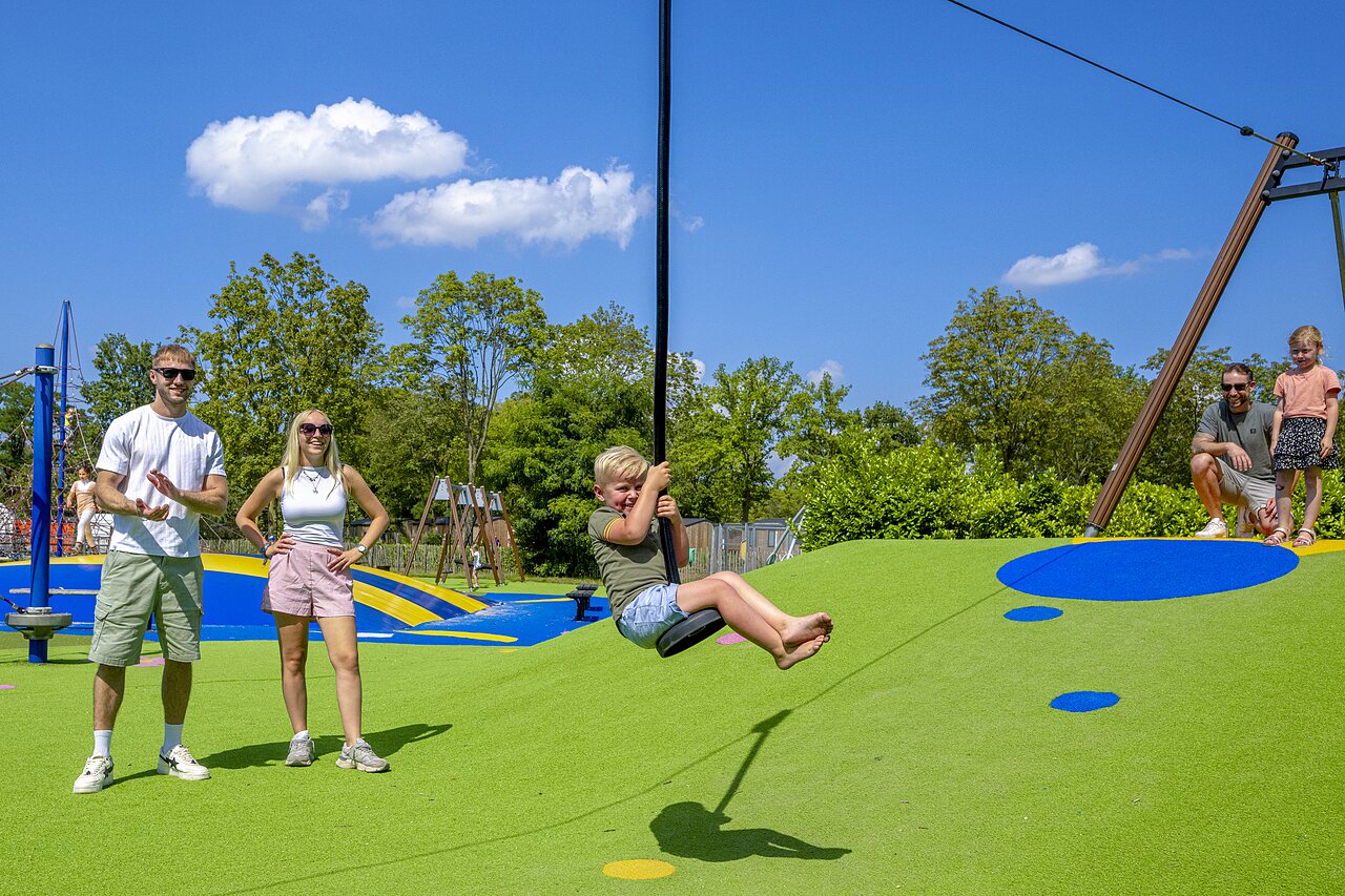 L�chelndes Kind an moderner Seilrutsche auf dem Spielplatz des Campingplatzes CAPFUN de Wondermolen in Molenschot.