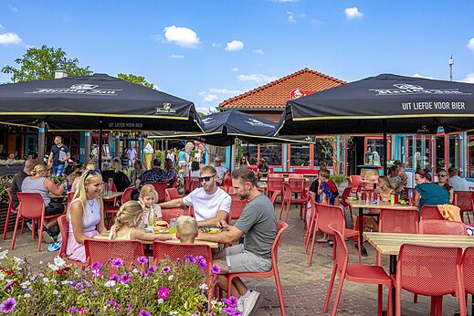 Lebhafte Restaurantterrasse mit Familien und Sonnenschirmen auf dem Campingplatz CAPFUN Wondermolen in Molenschot.
