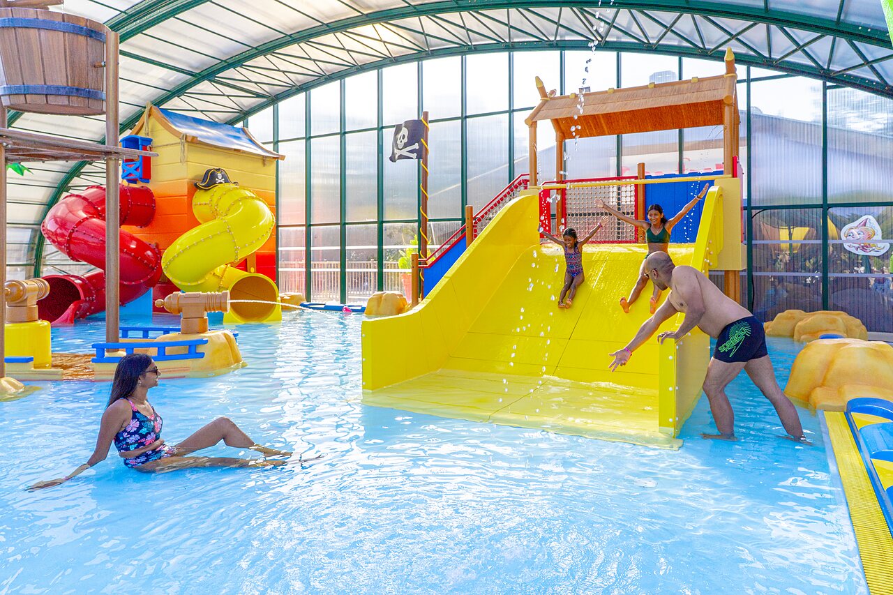 �berdachtes Schwimmbad mit Rutschen und Wasserspielen, Familie am�siert sich auf dem Campingplatz CAPFUN Zagarella in LONGEVILLE SUR MER (85).