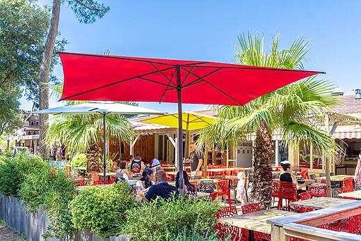 Außenterrasse des Restaurants mit bunten Sonnenschirmen und Gästen auf dem Campingplatz CAPFUN Zagarella in LONGEVILLE SUR MER (85).