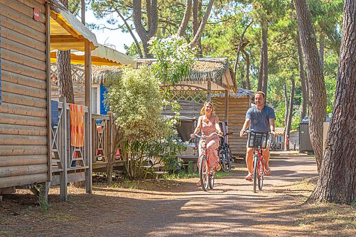 Paar f�hrt Fahrrad auf Weg zwischen Mobilheimen im Wald auf dem Campingplatz CAPFUN Zephir in Les Mathes La Palmyre (17).